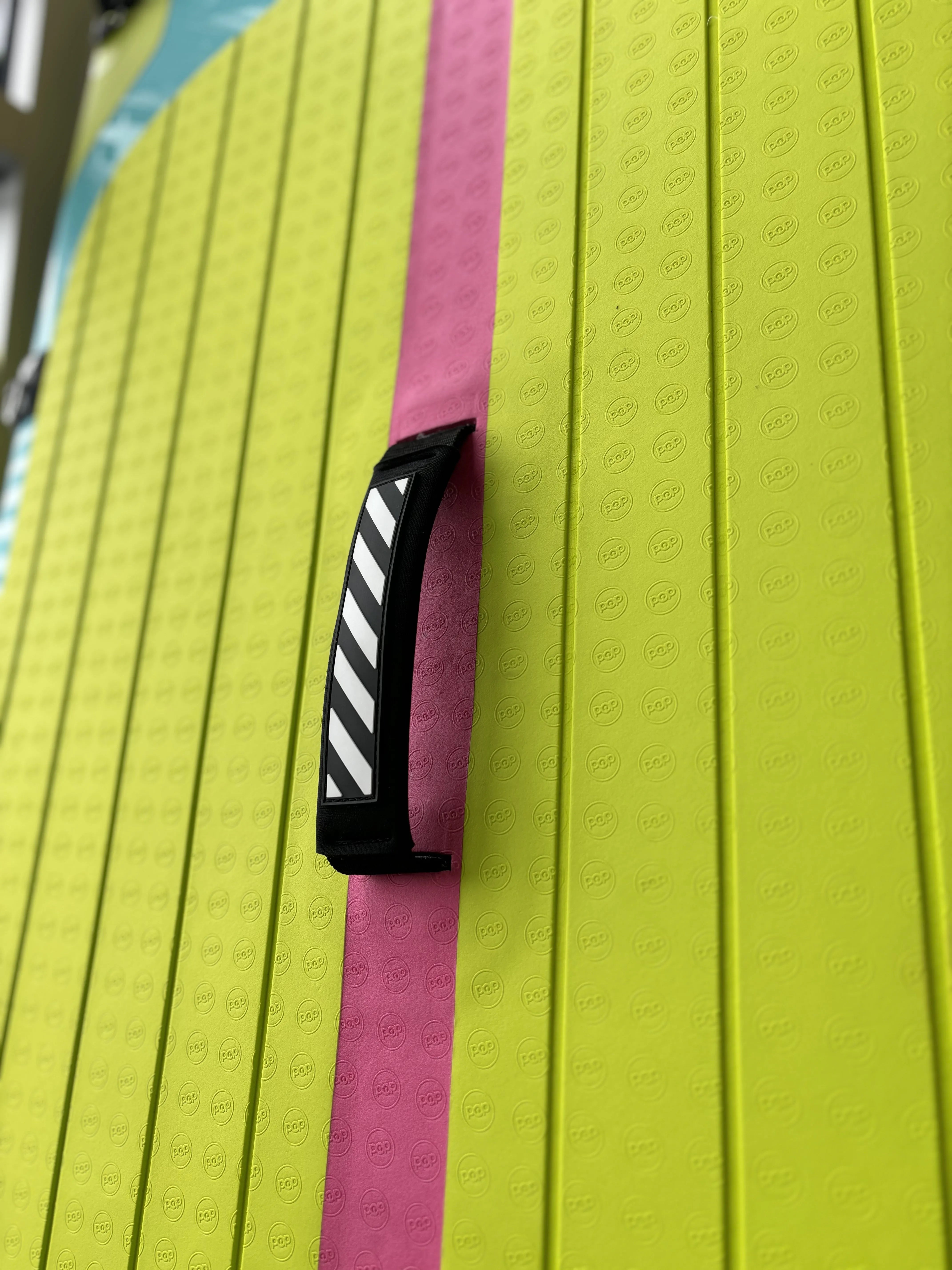 Close-up of the center carry handle on the Yacht Hopper paddleboard, showing the black and white diagonal stripe design against a textured neon yellow and pink deck pad.