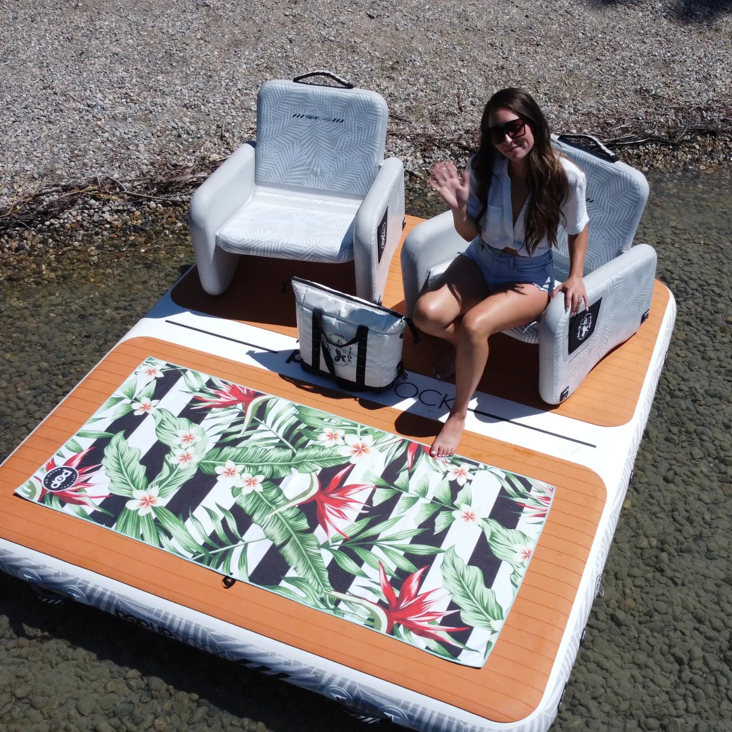 Woman relaxing on the POP Dock and Chair Bundle with inflatable chairs and beach towel setup on the water.