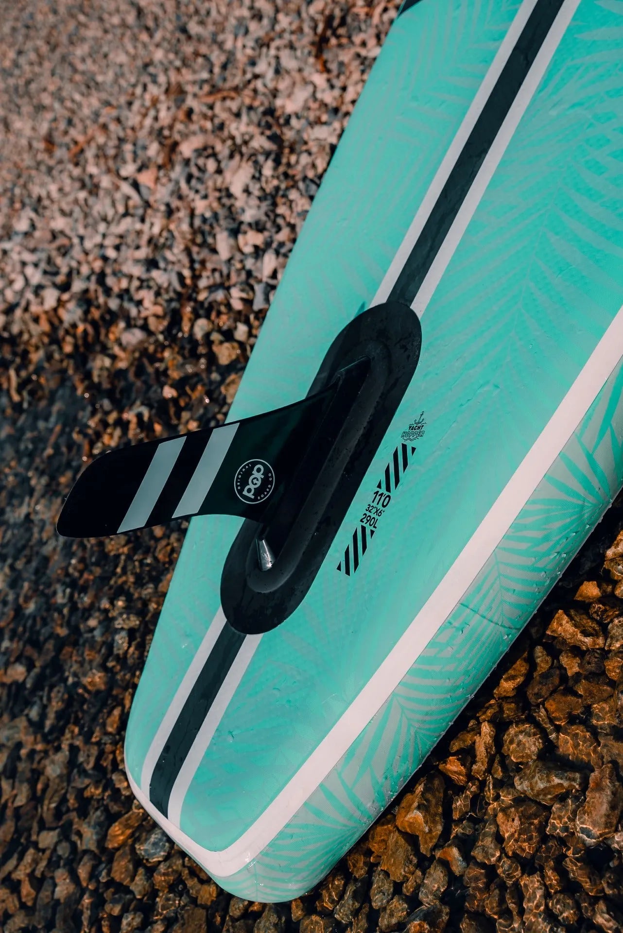 Close-up of the underside of the 11'0" Yacht Hopper inflatable paddleboard, showing the black detachable center fin, fin box, and board specifications (11'0 x 32" x 6") printed on the mint green hull.